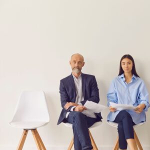 older male job candidate and younger female job candidate sit on white chairs