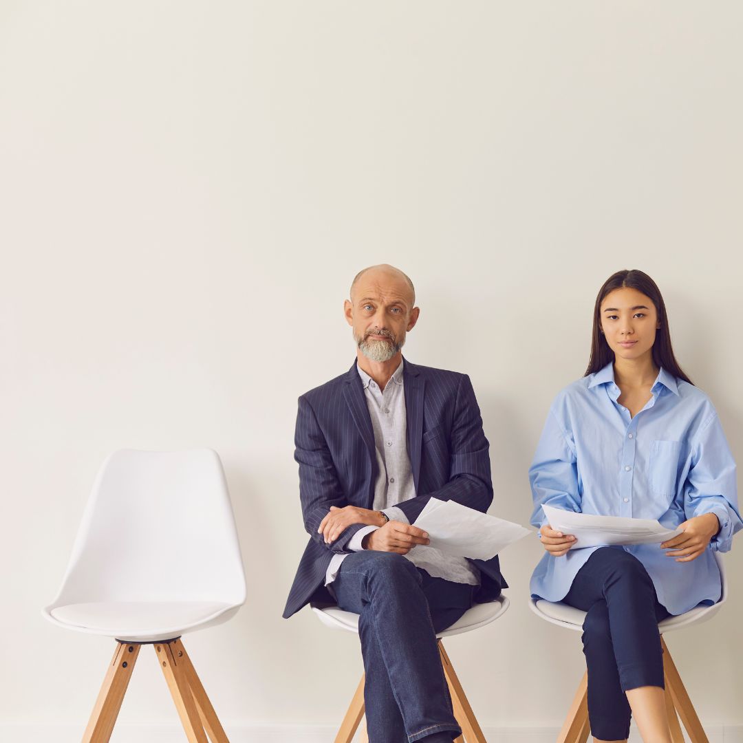 Blog post older male job candidate and younger female job candidate sit on white chairs